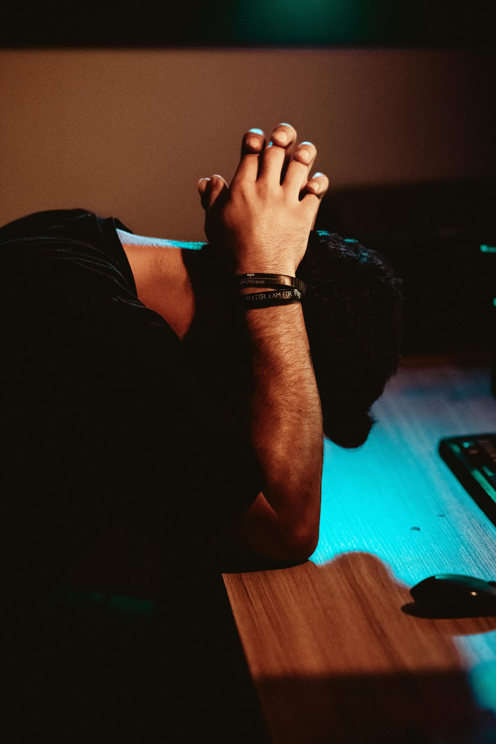 Man showing stress and exhaustion, leaning on a desk under dim lighting.