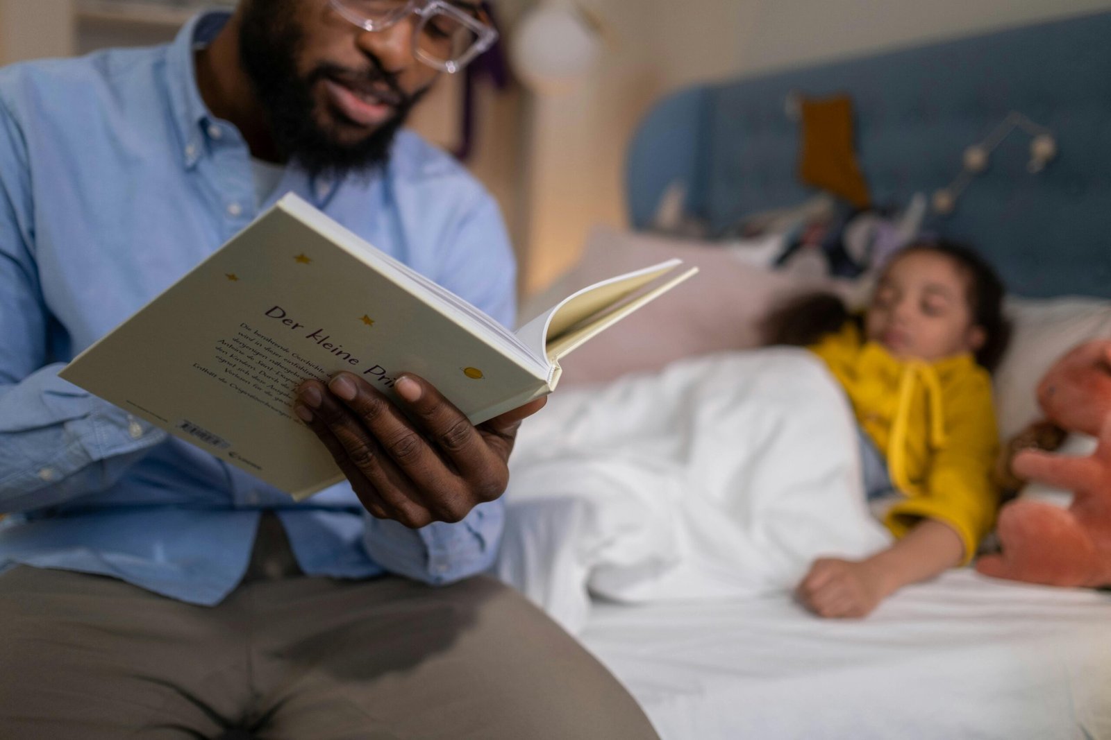 A father reading a bedtime story to his daughter, who is lying in bed, creating a warm and cozy atmosphere.