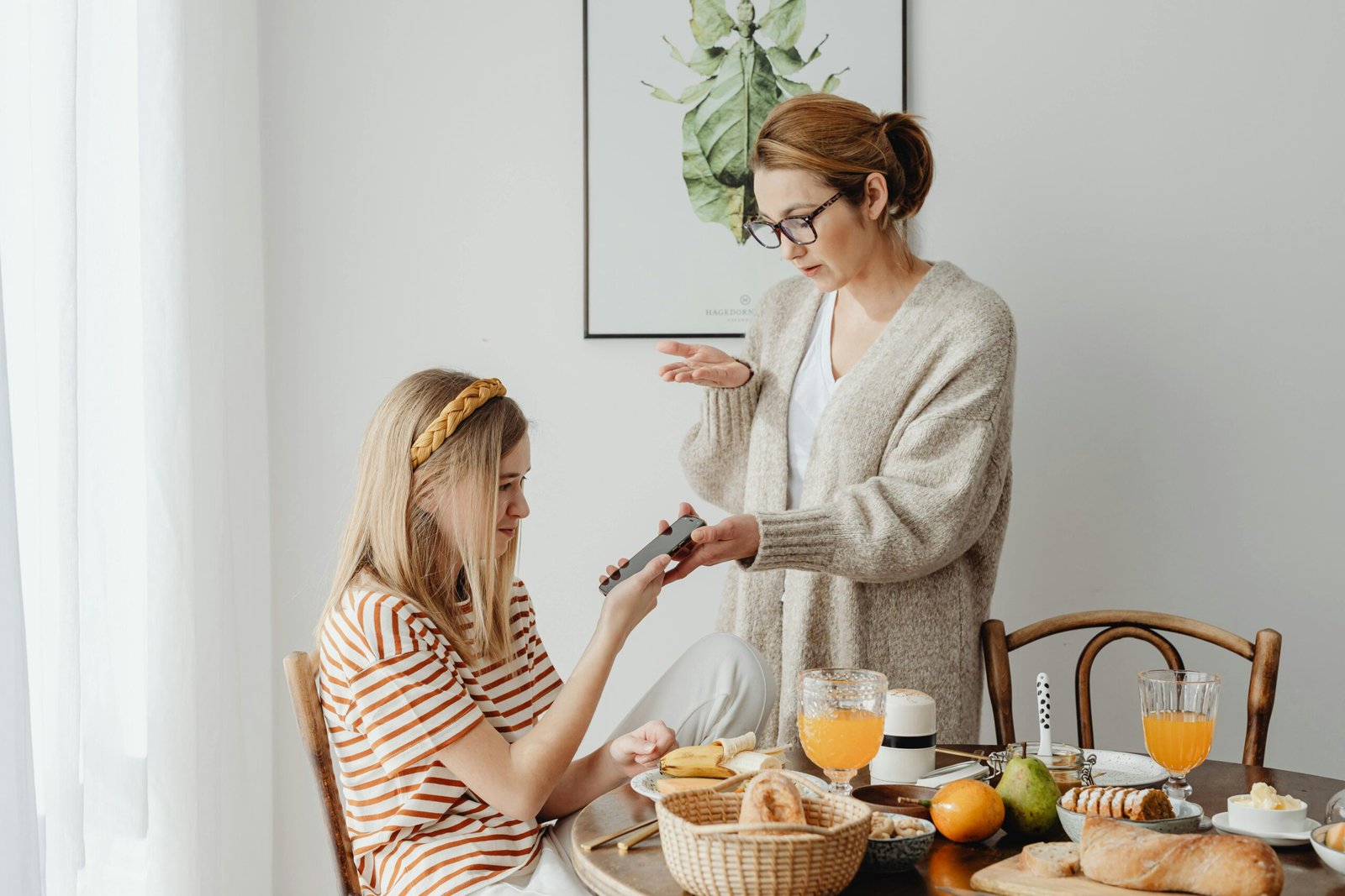 A mother and daughter in a discussion over phone use during breakfast at home.