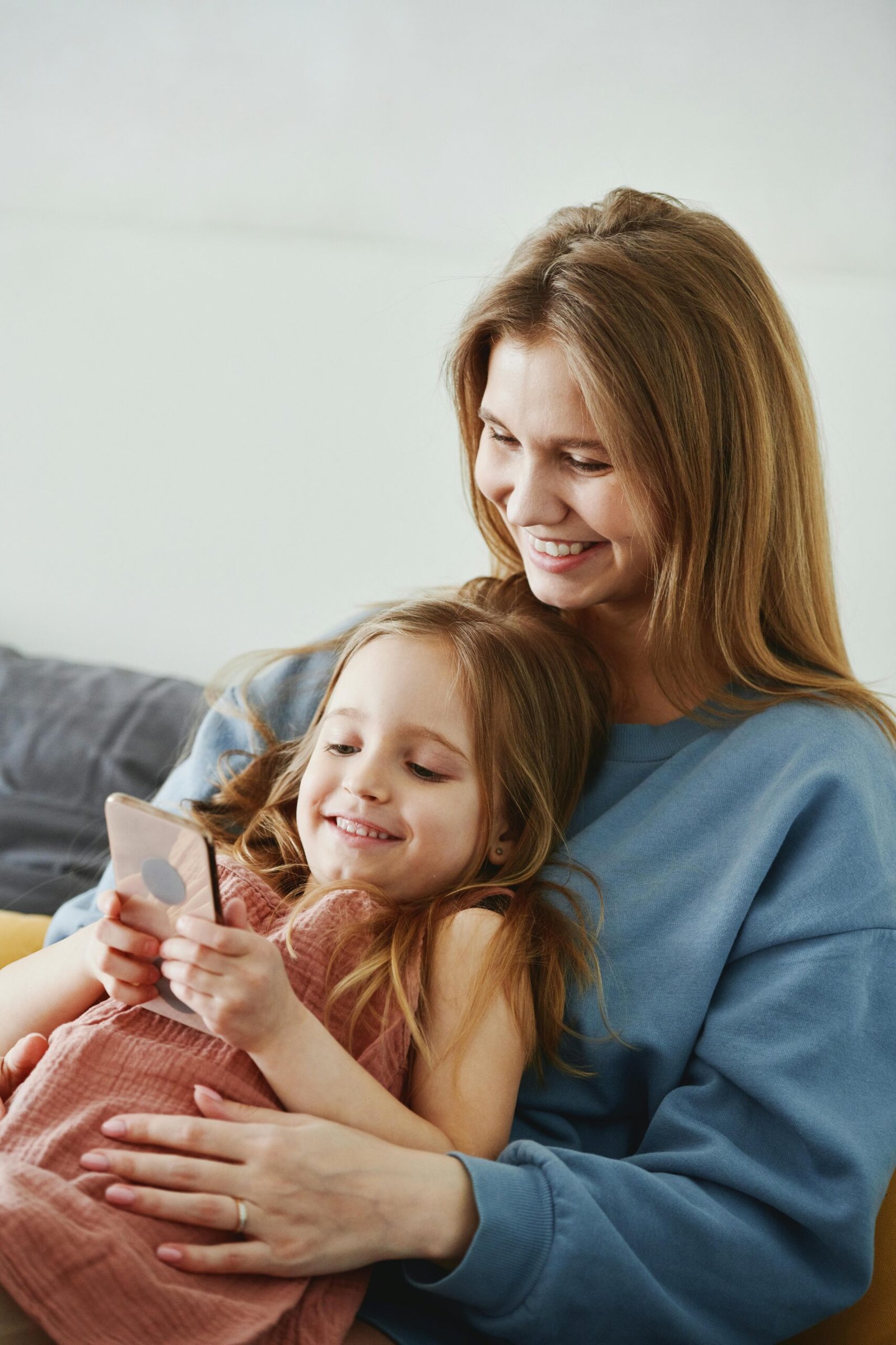 Caucasian mother and daughter smiling and using a smartphone at home, creating cherished family moments.