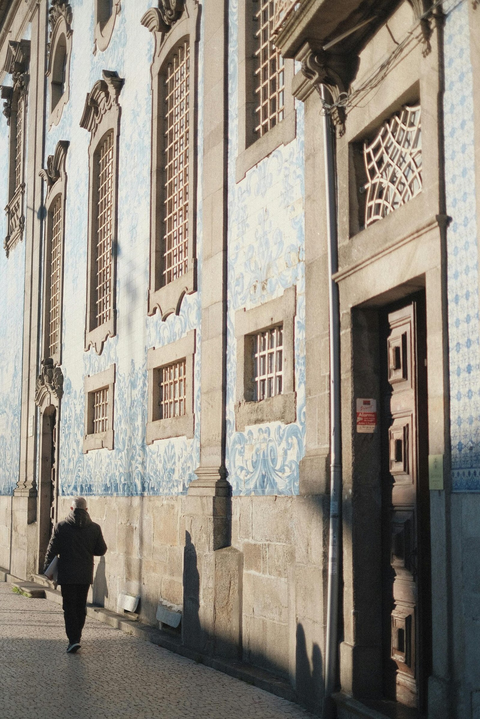 A person walks along a sunlit street by a historic building adorned with traditional tiles.