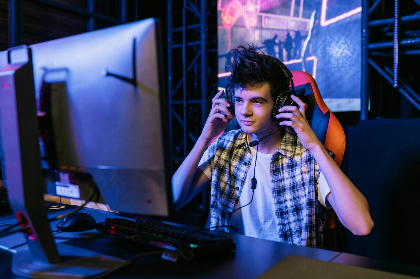 Teenage boy gaming at a computer station with headset during e-sports event.