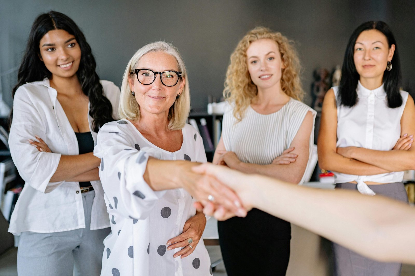 Diverse group of women in an office setting shaking hands and smiling, symbolizing partnership.