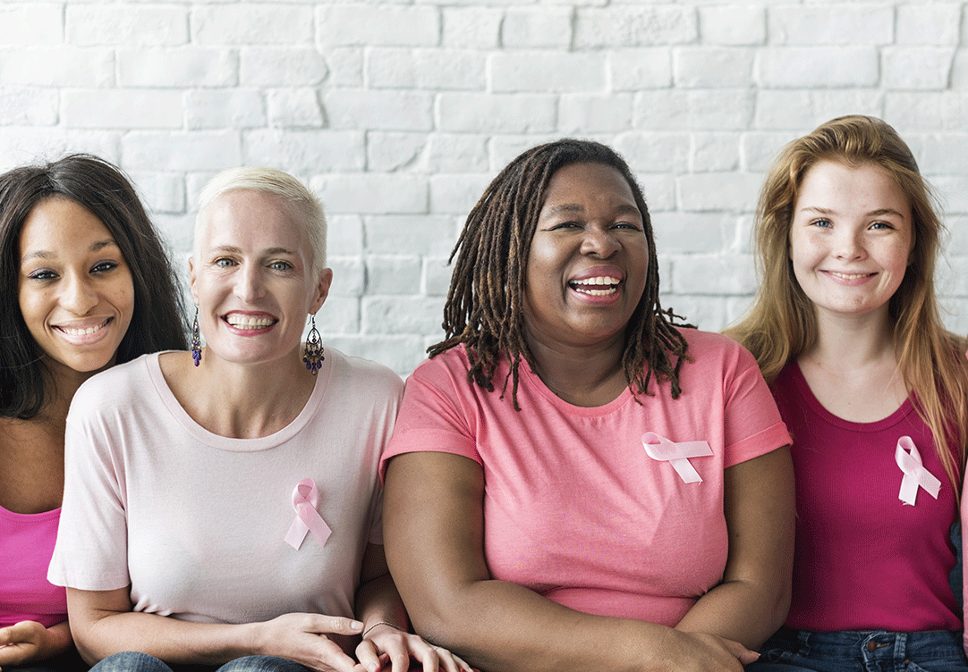 quatro mulheres de idades e etinias diferentes sentads e sorrindo vestindo rosa